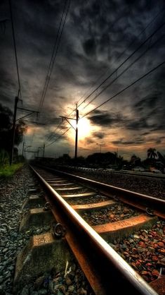 the sun is setting over train tracks with power lines in the foreground and dark clouds above