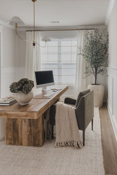 a desk with a computer on top of it in front of two chairs and a potted plant