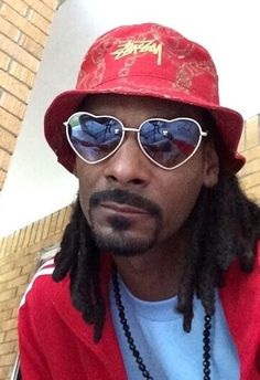 a man with dreadlocks wearing a red hat and sunglasses is looking at the camera