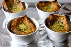 four small white bowls filled with food on top of aluminum foil