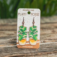 a pair of earrings featuring a plant in a pot on top of a wooden table