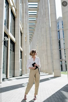 a woman in white shirt and khaki pants standing on sidewalk next to columns