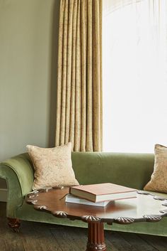 a green couch sitting in front of a window next to a table with books on it