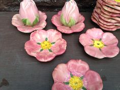 pink and yellow flowers are sitting next to each other on a wooden table with stacks of plates in the background