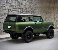 a green and black jeep parked on the side of a road next to a stone wall