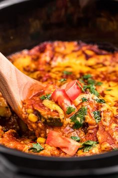 a wooden spoon in a skillet filled with chili and cheese covered casserole