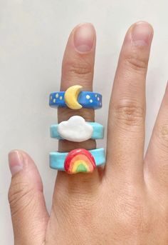 a person's hand holding three rings with rainbows, clouds and stars on them