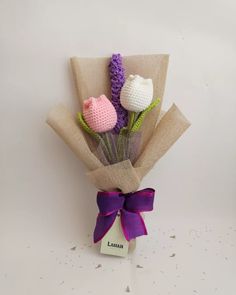 three crocheted flowers are wrapped in burlap and tied with a purple ribbon