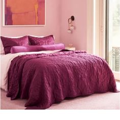 a bed with purple comforter and pillows in a room next to a painting on the wall