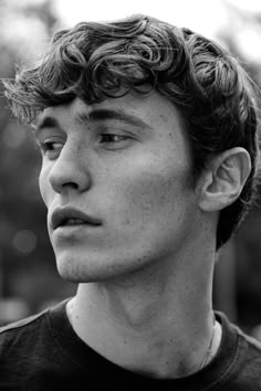 a young man with curly hair looks off to the side while wearing a black t - shirt