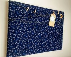 a blue wall hanging with clothes pins attached to it and a tag on the string