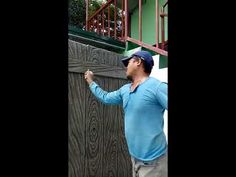 a man in blue shirt and hat leaning on fence with his hand up to the side