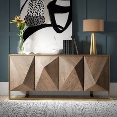 a sideboard with an abstract painting on the wall behind it and a vase filled with flowers