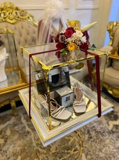 a display case with shoes and flowers in it on top of a marble table next to two chairs