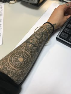 a person sitting at a desk with a laptop computer and a tattoo on their arm