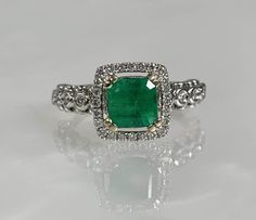 an emerald and diamond ring set in white gold with diamonds on the sides, sitting on a reflective surface