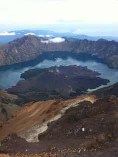 the view from top of a mountain looking down on a lake and mountains in the distance