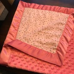 a pink blanket with polka dots on it sitting on a wooden table next to a chair