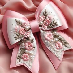 a pink and white bow with flowers on it's side, laying on a satin fabric