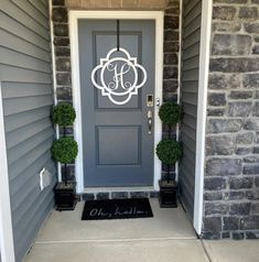 a gray front door with two potted topiary's and a monogrammed wreath