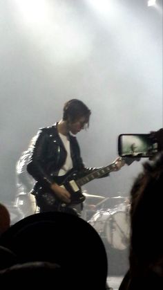 a man with a guitar standing in front of a mirror on stage at a concert