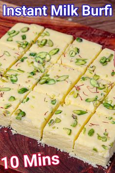 a wooden cutting board topped with lots of white frosted cake squares covered in pistat