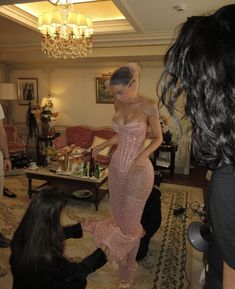 a woman in a pink dress standing next to two other women and one man sitting on the floor