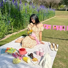 a woman sitting on top of a white blanket holding a baby next to purple flowers