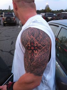 a man with a cross tattoo on his arm is standing next to a parked car