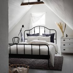 an attic bedroom with white walls and black iron bed frame, rugs on the floor