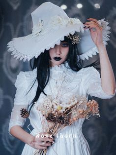 a woman with long black hair wearing a white hat and holding flowers in front of her face