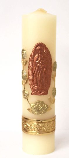 a white candle with gold trim and an image of the virgin mary on it's side