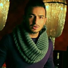 a man with a scarf around his neck looking at the camera while standing in front of some lights