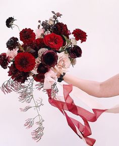 a woman holding a bouquet of flowers with red and white ribbons around her neck,