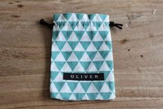 a teal and white pouch with the word oliver on it sitting on a wooden surface