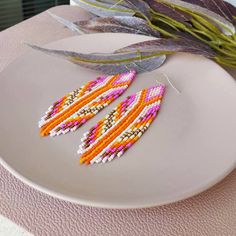 a pair of beaded earrings sitting on top of a plate next to a plant