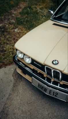 an old bmw is parked on the side of the road in front of some grass