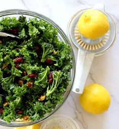 a glass bowl filled with kale salad next to two lemons