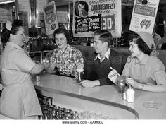 three women and one man are sitting at the bar talking to each other while another woman is holding a drink