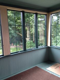 a room with three windows and a yoga mat on the floor in front of it