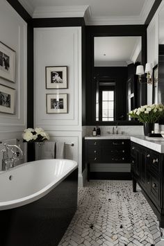 a black and white bathroom with an oval bathtub, double sinks, marble counter tops, and framed pictures on the wall