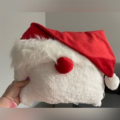 a hand holding a white stuffed animal with a red nose wearing a santa claus hat