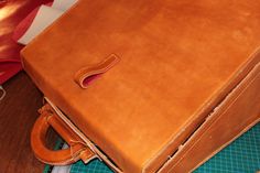 a brown leather briefcase sitting on top of a wooden table next to a red pillow