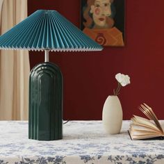 a green lamp sitting on top of a table next to an open book and vase