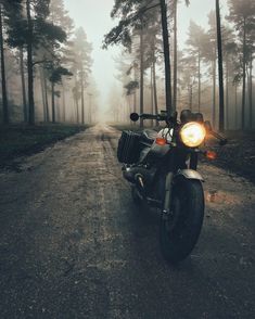 a motorcycle parked on the side of a dirt road in front of some tall trees