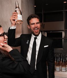 a man in a suit and tie holding a bottle of champagne to another woman's face