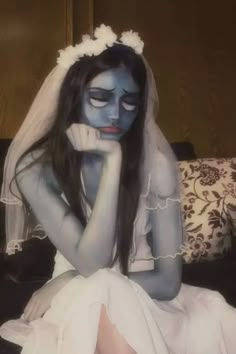 a woman in white dress sitting on bed with blue painted face and hands behind her head