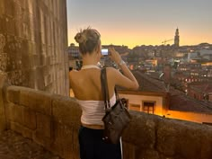 a woman standing on top of a stone wall next to a tall building with a clock tower in the background