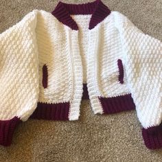 a white and maroon knitted jacket laying on the floor