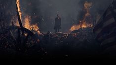 a man standing on top of a pile of fire next to an american flag